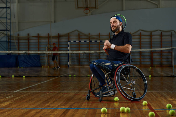 Молодий чоловік у інвалідному візку грає в теніс на корті
 - Фото, зображення