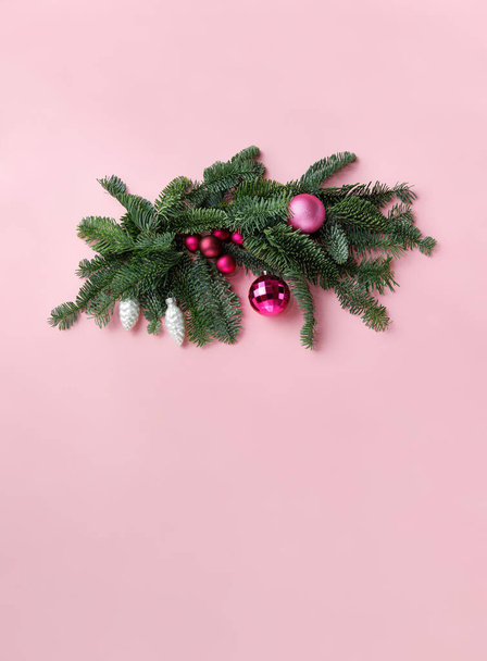 Рождественский флористический состав натуральных еловых ветвей (благородная ель), розовые рождественские шары и стеклянные конусообразные игрушки. Композиция выполнена на бледно-розовом фоне. Пространство для текста остается на заднем плане - Фото, изображение