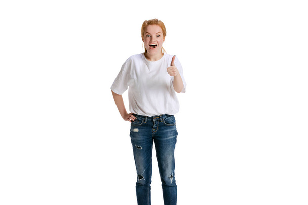 Cropped portrait of young excited girl rising thumb up, showing gesture of like, pleasure isolated over white background - 写真・画像