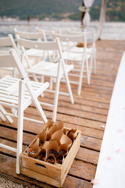 İçinde çiçek yaprakları olan bükülmüş zarflar olan kutu beyaz sandalyelerin yanında duruyor. - Fotoğraf, Görsel