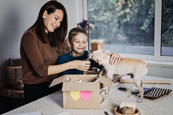 Szczęśliwa mama i dziecko wkładają kości do Pudełka Pet Subscription Box dla psów. Chihuahua pies i pudełko na prenumeratę zwierząt domowych z ekologicznych smakołyków, Zabawka, Kije Bully, All-Natural Chews sezonowych narzędzi - Zdjęcie, obraz