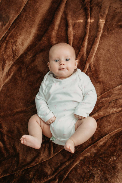 Yeni doğmuş organik pamuklu bebek kıyafetleri. Yatağın üzerinde duran organik pamuktan yapılmış beyaz tulumlu şirin bir bebek. Doğal tonlar, unisex bebek kıyafetleri. - Fotoğraf, Görsel