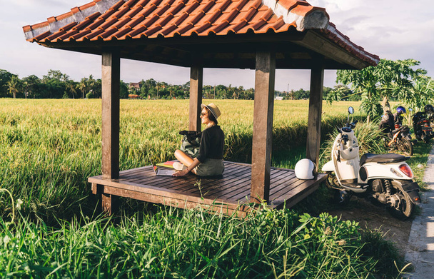 Caucasian female digital nomad in casual wear resting in gazebo enjoying solo travelling via vintage motorbike, young millennial hipster girl with modern laptop computer doing distance job - Fotó, kép