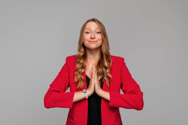 Coy young blonde woman begging for help, apologizing, say please with beg pray gesture, need something, standing in red blazer against gray background - Zdjęcie, obraz