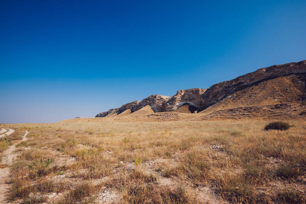 Picturesque view of empty rocky area with dry grass in desert valley in cloudless weather with blue sky during summer day - Foto, imagen