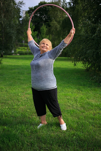 Señora mayor haciendo gimnasia con hula-hoop en el parque
 - Foto, imagen