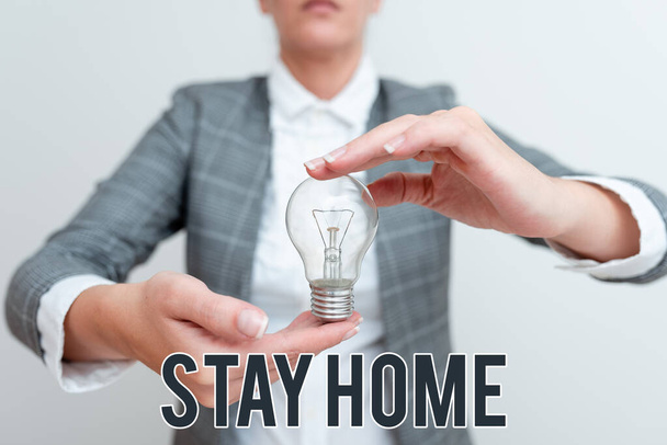 Znak tekstowy pokazujący Zostań w domu. Koncepcja oznacza nie wychodzić na działalność i pobyt w domu lub domu Lady w strój trzymając lampę z dwoma rękami prezentując nowe pomysły technologiczne - Zdjęcie, obraz