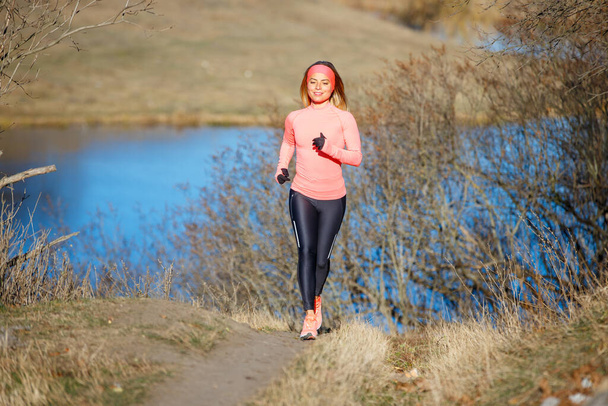 Young woman jogging in the park near the pond in the cold sunny morning - Foto, Bild