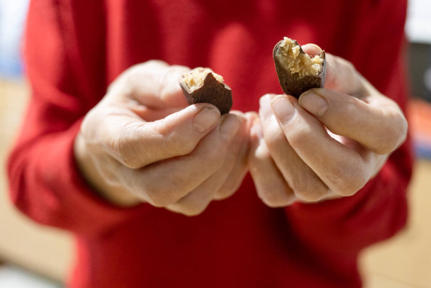 vooraanzicht van de handen van senior vrouw houden gebroken chocolade snoep (focus op het snoep op de voorgrond - Foto, afbeelding