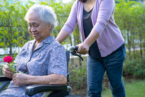介護娘抱擁とヘルプアジアのシニアまたは高齢者の女性保持赤いバラオン車椅子で公園. - 写真・画像