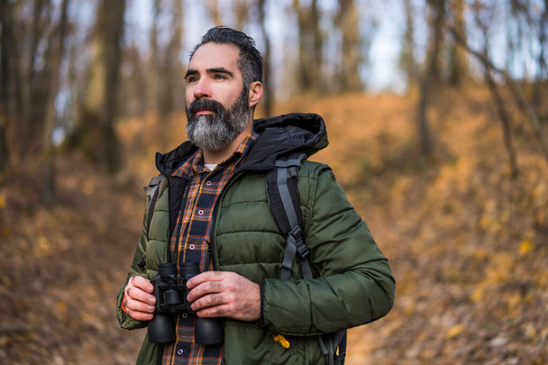 Image of man holding binoculars and looking at direction while hiking. - Photo, Image
