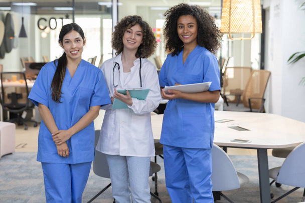 Νεαρή γυναικεία ιατρική ομάδα εργασίας φορώντας στολή εργασίας χαμογελώντας και κοιτάζοντας κάμερα. - Φωτογραφία, εικόνα