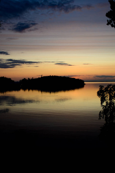Vertical photo of a beautiful sunset in Karelia over the silhouettes of the islands. Reflection of the island and sky in the water of Lake Ladoga - Фото, зображення