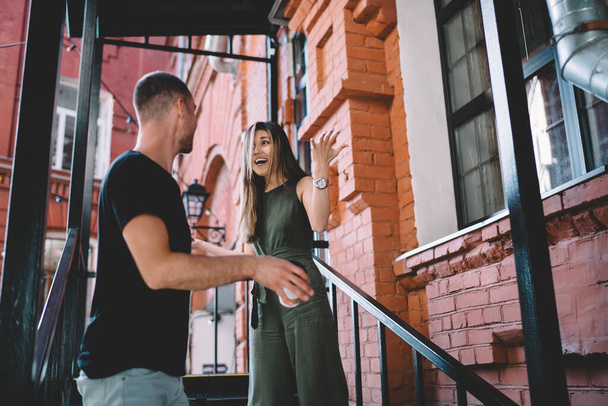 Low angle of distressed ethnic couple in casual clothes standing on staircase and having conflict while looking at each other - Фото, зображення