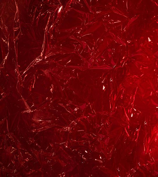 red rumpled foil or polyethylene on a red background. Hard light, facets of folds. Abstract background for design - Fotoğraf, Görsel