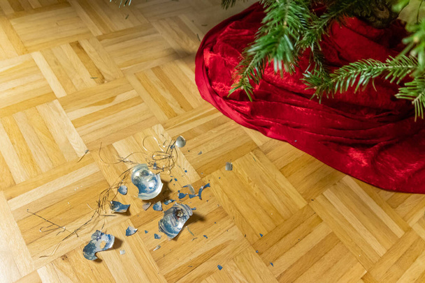 Bolas de Navidad rotas en el suelo fueron destruidas por los niños en la víspera santa durante la decoración del árbol de Navidad con la familia y tienen que ser barridos con escoba barrida para limpiar y adornar - Foto, imagen