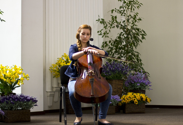 Giovane ragazza che suona il violoncello in una grande sala luminosa.Ritrae bella ragazza con i capelli lunghi. Strumenti musicali
 - Foto, immagini