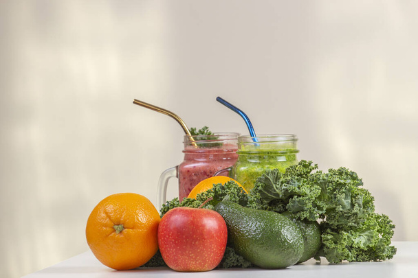 Batido de coquetel de bebida saudável em jarros de vidro com folhas de couve verdes frescas, abacates, maçã, cor-de-laranja na mesa branca. Alimentos vegetarianos veganos saudáveis - Foto, Imagem