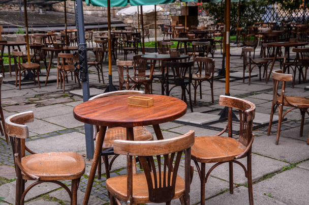 Leeres Straßencafé mit kleinen runden Tischen und Holzstühlen nach dem Regen am bewölkten Tag - Foto, Bild