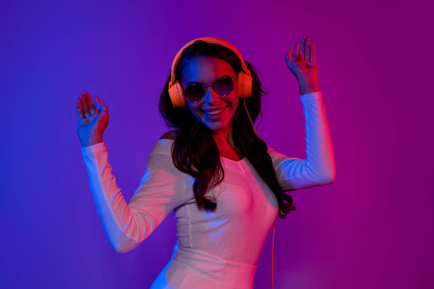 Photo of lovely millennial brunette lady listen music dance wearing headphones white dress eyewear isolated over neon color background - Fotó, kép