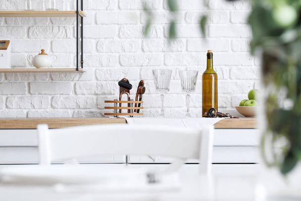 Empty glasses and bottle of wine on kitchen counter near white brick wall - Photo, image