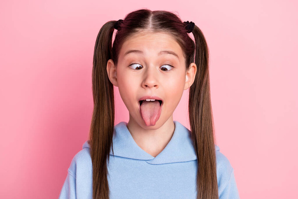 Photo portrait of funny schoolgirl showing tongue fooling grimacing isolated on pastel pink color background - Fotografie, Obrázek