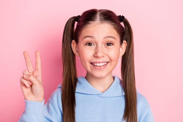 Photo portrait of happy schoolgirl showing v-sign gesture smiling in blue outfit isolated on pastel pink color background - Photo, Image