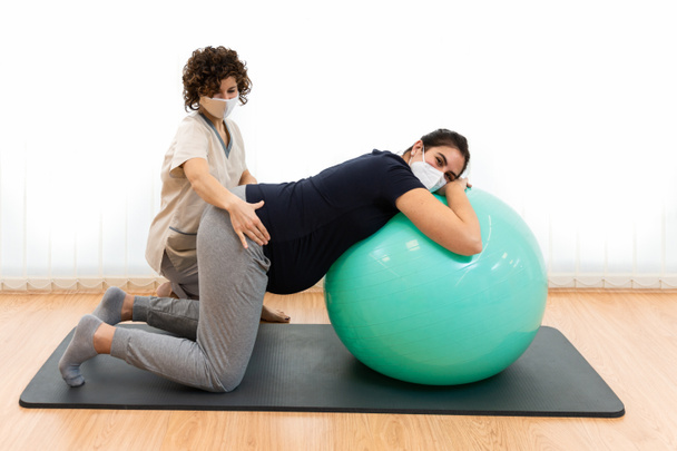 A pregnant woman doing pilates exercises with a ball with the help of her physiotherapist - Foto, Imagem