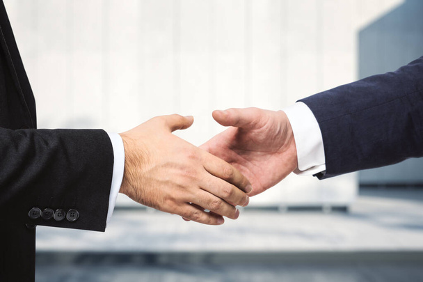 Two businessmen shake hands on the background of sunny exterior of the business center, deal concept, close up - Foto, Imagem