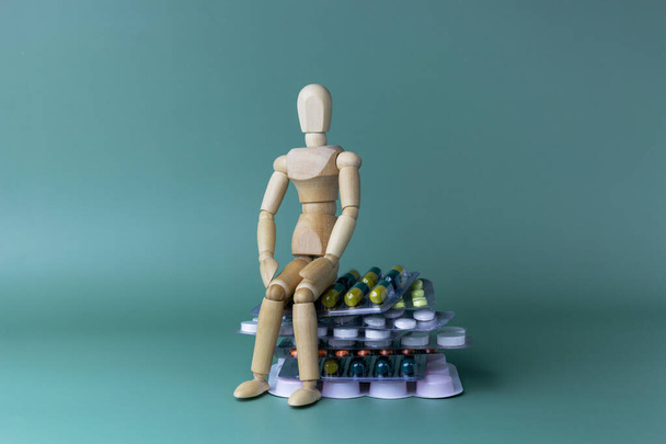 Modelo de juguete de un hombre de madera está sentado en pastillas. Concepto de salud. Copiar espacio. - Foto, Imagen