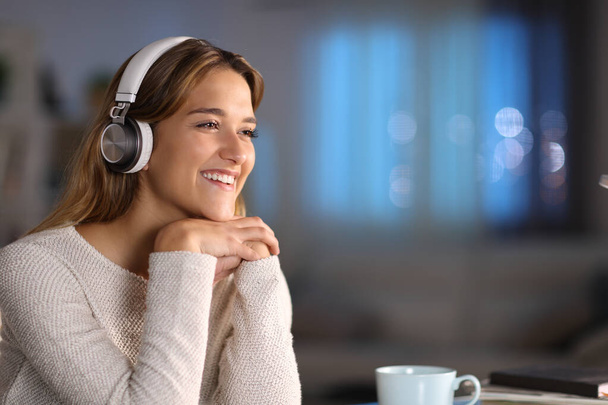 Happy woman wearing headphones smiling listening to music at home in the night - Fotoğraf, Görsel