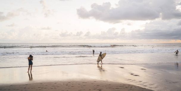 Unrecognizable group of people with surfboard strolling on wet beach near waving sea during vacation at sundown time on Bali - Fotografie, Obrázek