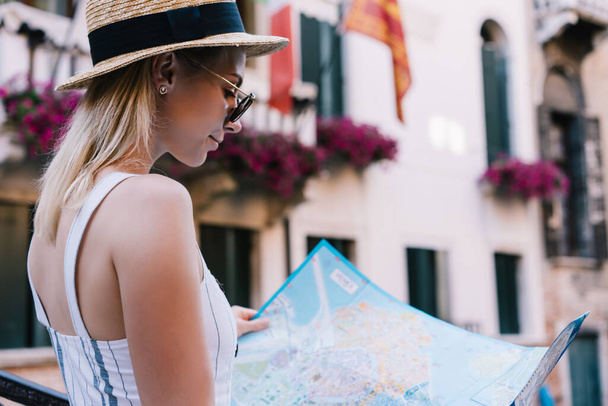 Side view of content lady standing outside vintage house and examining paper map while spending time in Venice in Italy - 写真・画像