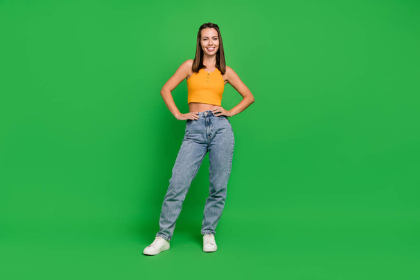 Full length photo of cool young brunette lady stand wear top jeans sneakers isolated on green color background - Fotografie, Obrázek