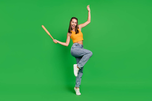 Full body photo of young funny brunette lady hold bit wear top jeans shoes isolated on green color background - Fotoğraf, Görsel