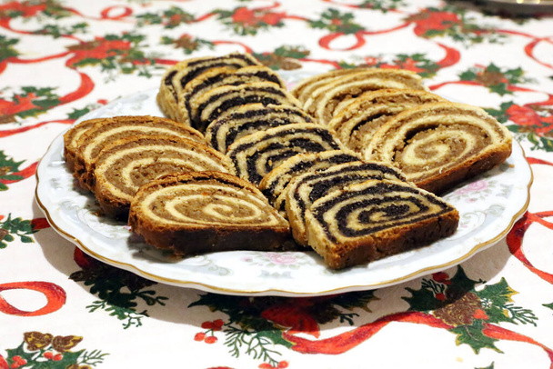 Kotitekoinen unikonsiemeniä tai saksanpähkinä roll kakkuja alias beigli tai bejgli viipaleita kuin siivekäs enkeli lautasella. Perinteinen unkarilainen joulu viipaloitu kakkuja pöydällä - Valokuva, kuva