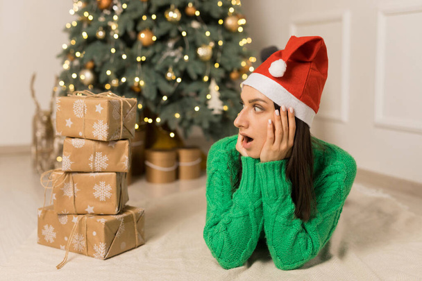 Το νεαρό έκπληκτο κορίτσι που κείτεται κοντά στο χριστουγεννιάτικο δέντρο και καφέ δώρα - Φωτογραφία, εικόνα