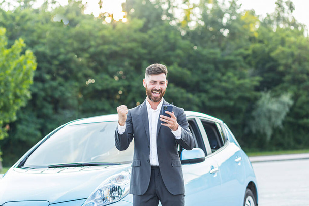 Successful businessman man rejoices in victory, man wins car in phone app, looks at phone and shouts of joy and euphoria of happiness - Φωτογραφία, εικόνα