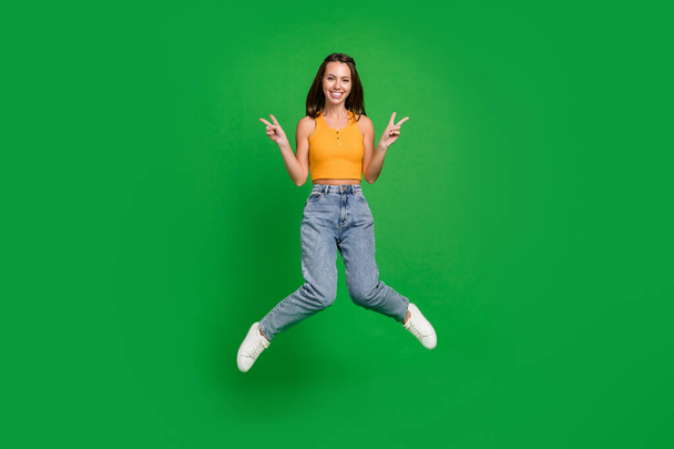 Фотографія повного тіла тисячоліття крута брюнетка леді стрибає носити верхні джинси взуття ізольовані на зеленому фоні
 - Фото, зображення