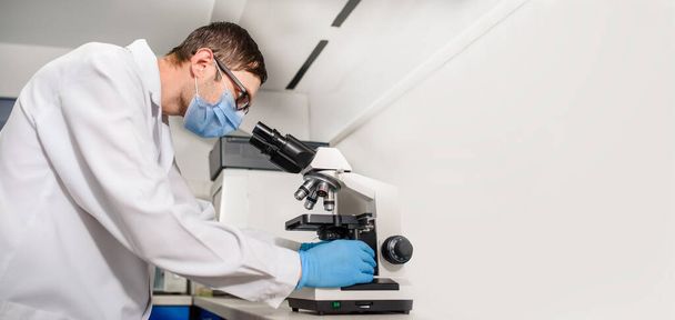 W laboratoriach szpitalnych pracuje proces, młody lekarz patrzy w mikroskop medyczny na badanie krwi. - Zdjęcie, obraz