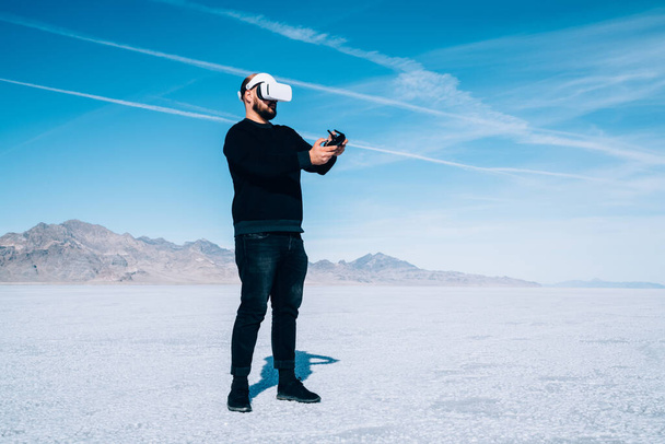 Full length unrecognizable male traveler in black clothes standing on empty salt flat in modern headset while exploring cyberspace on sunny day - Φωτογραφία, εικόνα