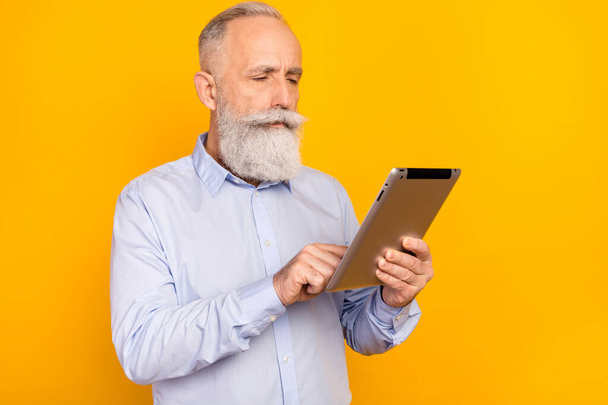 Photo of serious calm focused old man look hold tablet businessman isolated on yellow color background - Фото, изображение