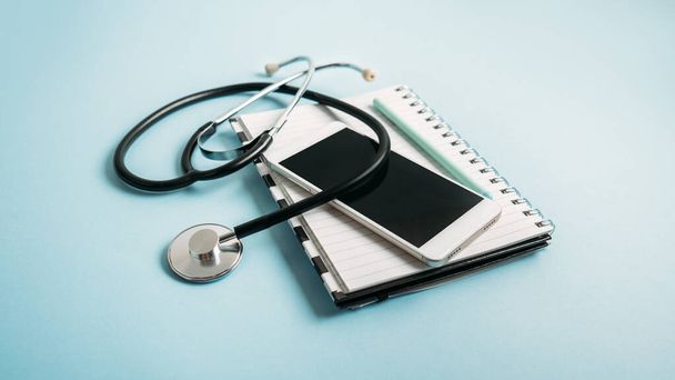 Телемедицина або віртуальний візит до телевізійного здоров'я, відео-відвідування, концепція віддаленого відео чату лікаря з смартфоном, відкрита блокнот і стетоскоп на синьому фоні
 - Фото, зображення