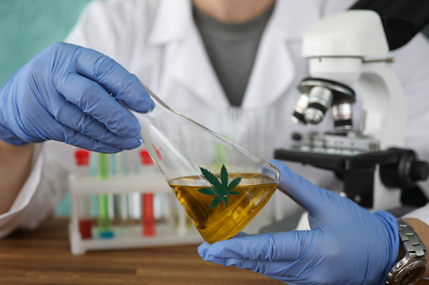 Kemisti hansikkaissa marihuaniöljyä sisältävä pullo lähikuvassa laboratoriossa - Valokuva, kuva