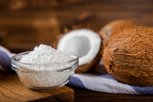 Coconut flakes in a bowl, coconuts on a wooden background. Close-up. - Fotografie, Obrázek