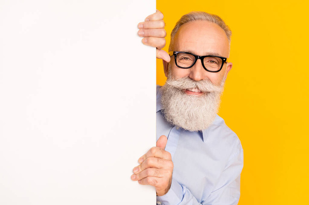 Photo of attractive charming old man hold hands whit board empty space isolated on yellow color background - Fotografie, Obrázek