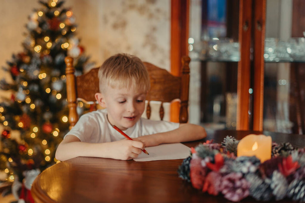 Kerst Child Write Letter to Santa Claus, Kid Writing Wenslijst, niet gerichte verlichting achtergrond. 6-jarige jongen schrijft een brief aan de Kerstman - Foto, afbeelding