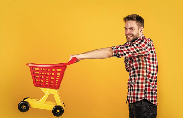 stylish male carry shopping cart. bearded man in shop store. buy and purchase. prepare for holidays. householding. real shopaholic. young guy in checkered shirt go shopping - Foto, Bild