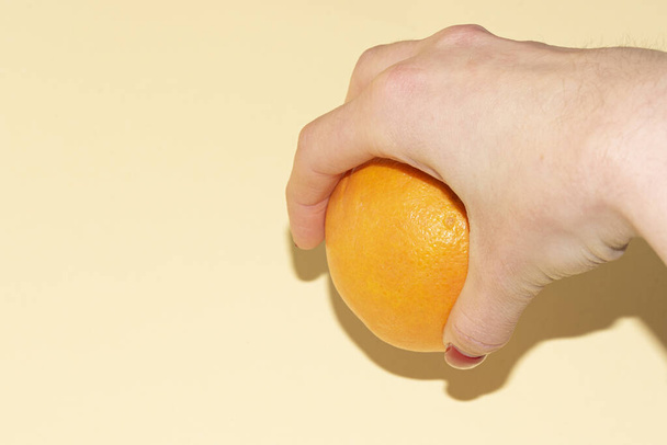 close-up shot of female hand with orange on light color background - Foto, Imagem