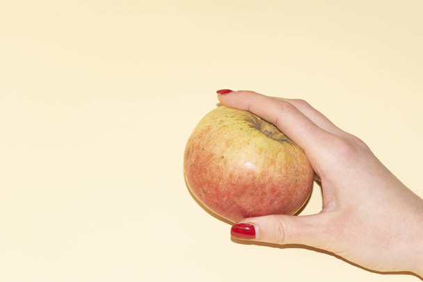 zbliżenie strzał żeńskiej ręki z jabłkiem na tle jasnego koloru - Zdjęcie, obraz